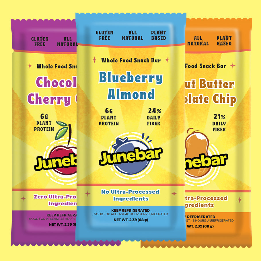 Three Junebar whole food snack bars shown in a row against a yellow background. The center bar is Blueberry Almond with a blue top band, and the side bars are Chocolate Cherry with a purple top band and Nut Butter Chocolate Chip with an orange top band.