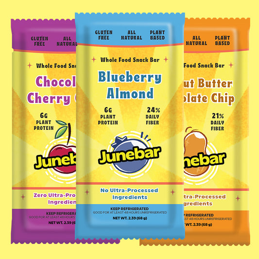 Three Junebar whole food snack bars shown in a row against a yellow background. The center bar is Blueberry Almond with a blue top band, and the side bars are Chocolate Cherry with a purple top band and Nut Butter Chocolate Chip with an orange top band.